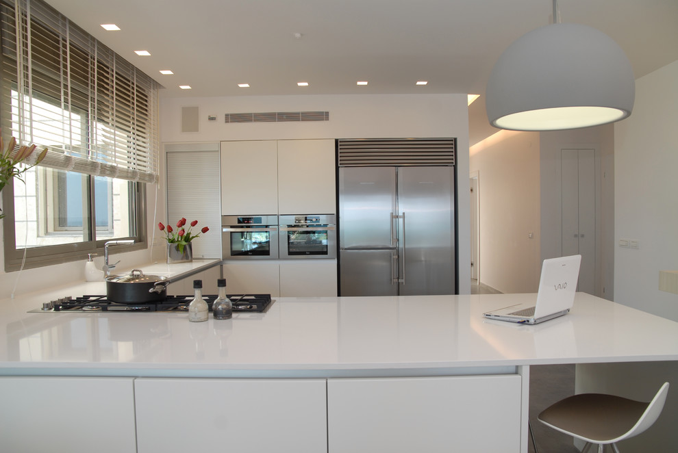 Coastal u-shaped open plan kitchen in Tel Aviv with stainless steel appliances, flat-panel cabinets, white cabinets, a built-in sink and composite countertops.