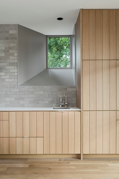 Exempel på ett modernt kök, med en undermonterad diskho, skåp i ljust trä, bänkskiva i kvarts, grått stänkskydd, stänkskydd i tegel, integrerade vitvaror och ljust trägolv