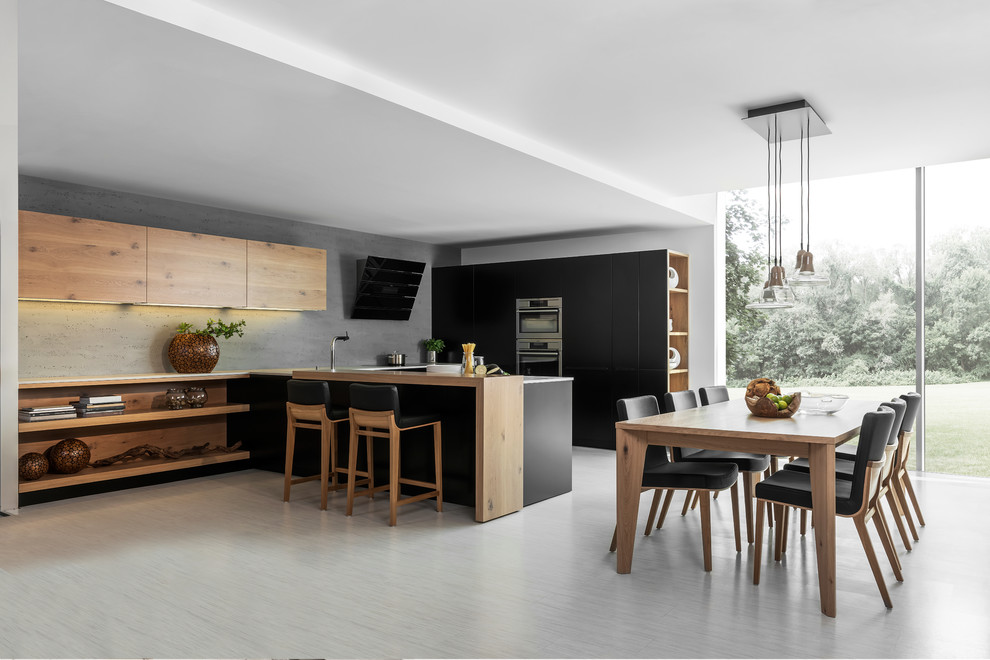 Modelo de cocina comedor lineal moderna grande con electrodomésticos de acero inoxidable, península, armarios con paneles lisos y puertas de armario de madera clara