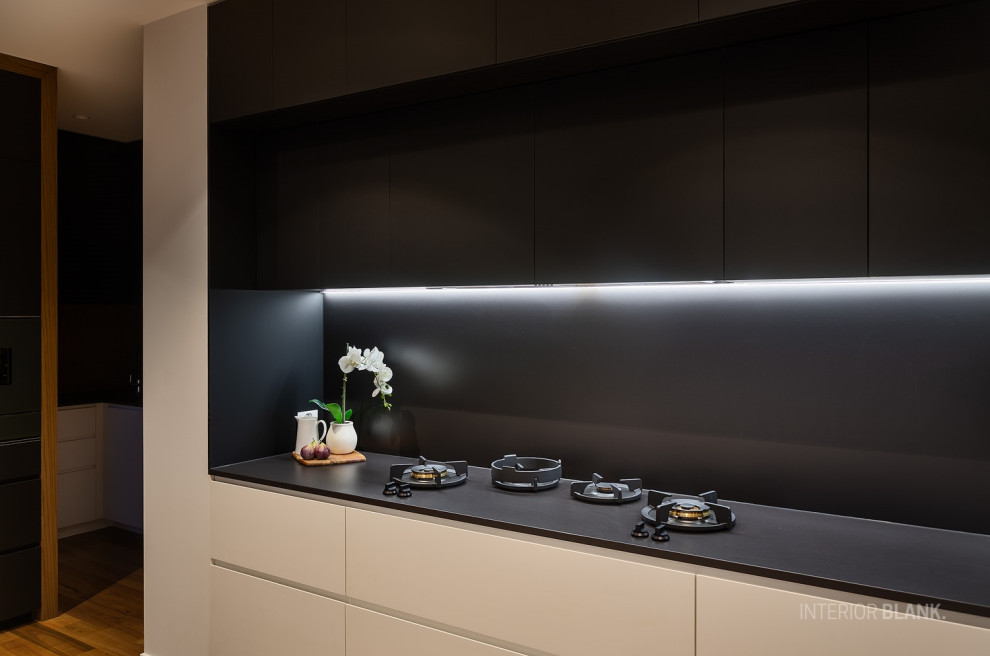 Modern inredning av ett mycket stort svart svart kök med öppen planlösning, med en undermonterad diskho, släta luckor, vita skåp, bänkskiva i koppar, svart stänkskydd, stänkskydd i sten, svarta vitvaror, mellanmörkt trägolv och en köksö