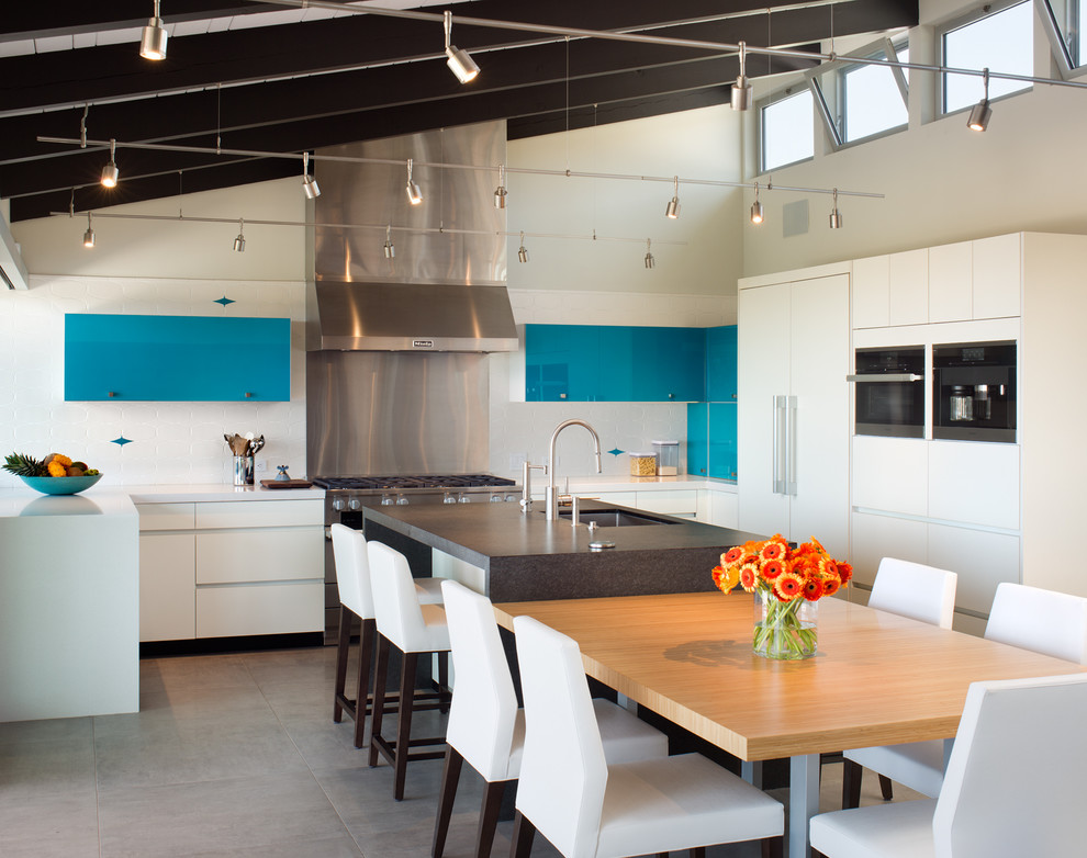 Bild på ett funkis kök, med en undermonterad diskho, släta luckor, vita skåp, blått stänkskydd, svarta vitvaror, en köksö och grått golv