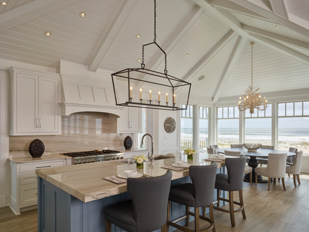 This is an example of an expansive coastal kitchen/diner in Philadelphia with recessed-panel cabinets, white cabinets, marble worktops, beige splashback, marble splashback, stainless steel appliances, medium hardwood flooring, an island, beige worktops and a vaulted ceiling.