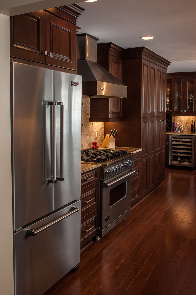 Example of a classic galley eat-in kitchen design in Detroit with an undermount sink, raised-panel cabinets, brown cabinets, granite countertops, brown backsplash, stone tile backsplash and stainless steel appliances