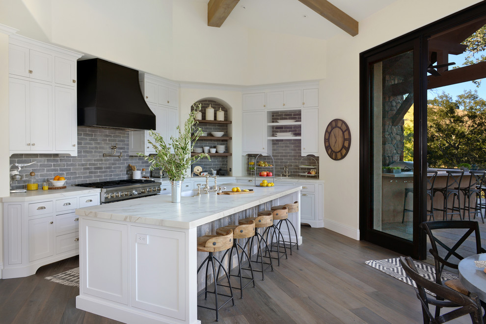 Inspiration for a mediterranean kitchen/diner in San Francisco with a single-bowl sink, shaker cabinets, white cabinets, grey splashback, stainless steel appliances, an island and brown floors.