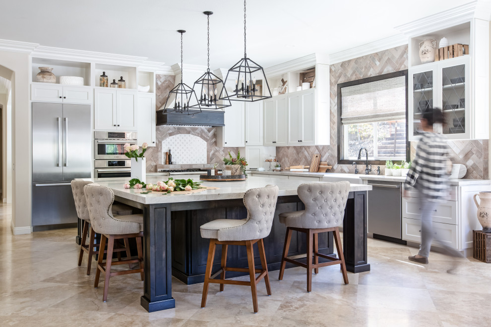 Open concept kitchen - large traditional l-shaped travertine floor and beige floor open concept kitchen idea in San Diego with a farmhouse sink, shaker cabinets, quartzite countertops, stainless steel appliances, an island, white cabinets, gray backsplash and white countertops