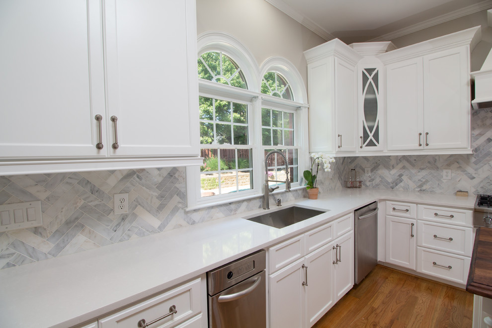 Inspiration for a mid-sized transitional l-shaped medium tone wood floor eat-in kitchen remodel in Atlanta with an undermount sink, shaker cabinets, white cabinets, quartzite countertops, white backsplash, stone tile backsplash, stainless steel appliances and an island