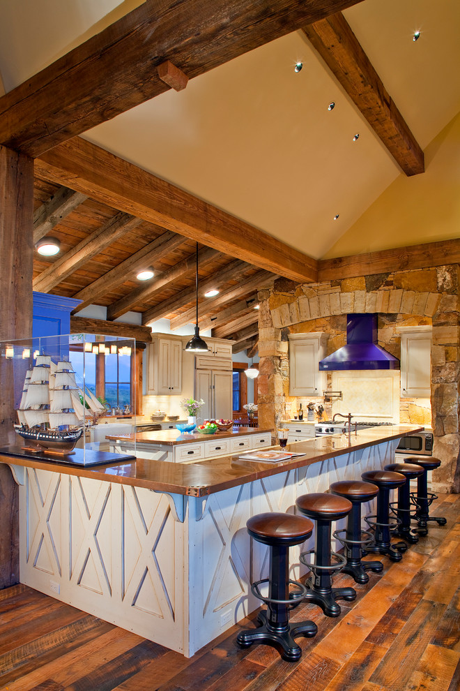 Imagen de cocina rural con puertas de armario beige, salpicadero beige, electrodomésticos con paneles y pared de piedra