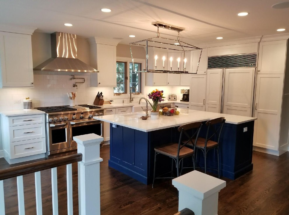 Klassisk inredning av ett l-kök, med en rustik diskho, luckor med infälld panel, blå skåp, rostfria vitvaror, mellanmörkt trägolv, en köksö och brunt golv