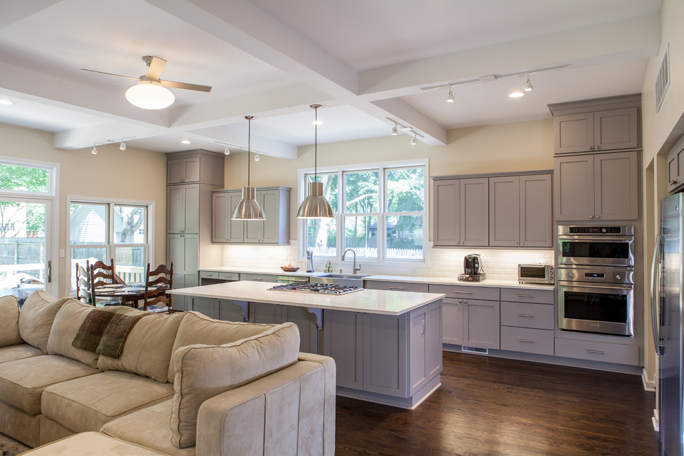 Large traditional l-shaped open plan kitchen in Chicago with grey cabinets, an island, a belfast sink, shaker cabinets, engineered stone countertops, white splashback, metro tiled splashback, stainless steel appliances and dark hardwood flooring.