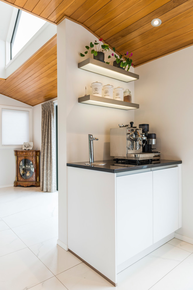 Design ideas for a medium sized contemporary galley kitchen pantry in Christchurch with a submerged sink, flat-panel cabinets, white cabinets, engineered stone countertops, grey splashback, glass sheet splashback, stainless steel appliances, ceramic flooring, an island and white floors.