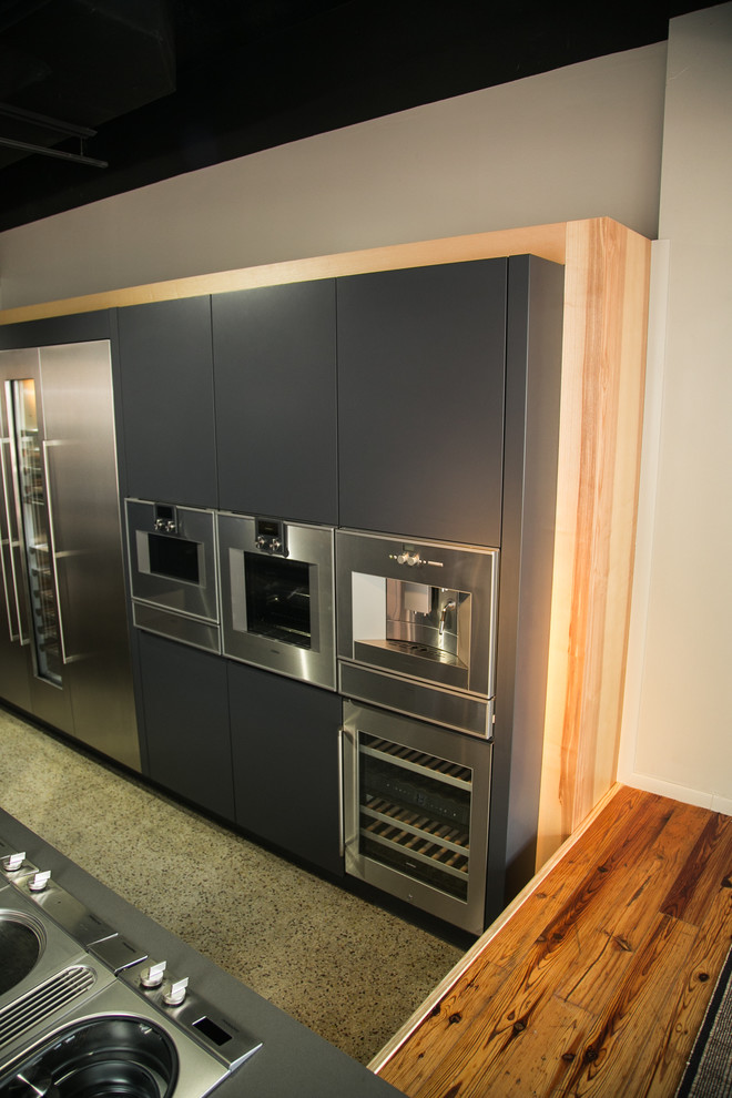 Modelo de cocina actual pequeña abierta con armarios con paneles lisos, puertas de armario grises, encimera de madera, electrodomésticos de acero inoxidable, suelo de linóleo y una isla