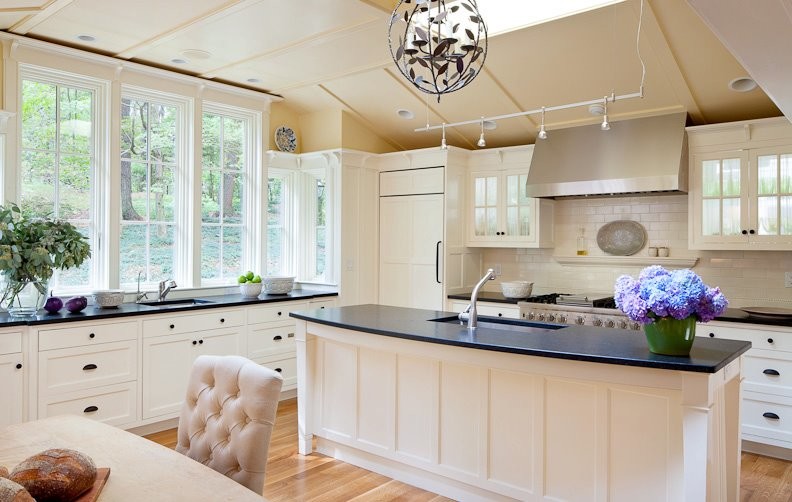 Inspiration for a mid-sized timeless l-shaped medium tone wood floor eat-in kitchen remodel in Boston with an undermount sink, glass-front cabinets, white cabinets, granite countertops, white backsplash, paneled appliances, an island, ceramic backsplash and black countertops