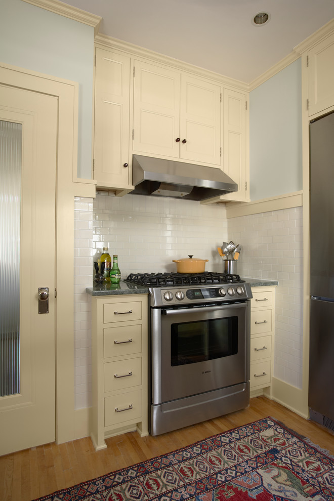 Exempel på ett avskilt klassiskt u-kök, med luckor med infälld panel, gula skåp, vitt stänkskydd, stänkskydd i tunnelbanekakel, rostfria vitvaror och ljust trägolv