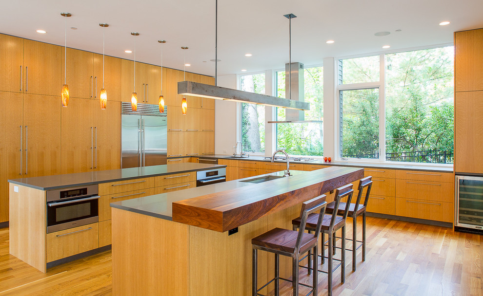 Eat-in kitchen - mid-sized modern l-shaped light wood floor and beige floor eat-in kitchen idea in DC Metro with an undermount sink, flat-panel cabinets, medium tone wood cabinets, solid surface countertops, stainless steel appliances, two islands and black countertops