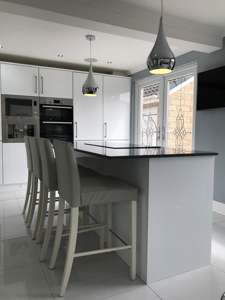 Medium sized contemporary single-wall open plan kitchen in Glasgow with flat-panel cabinets, white cabinets, quartz worktops, stainless steel appliances, ceramic flooring, an island, white floors and black worktops.