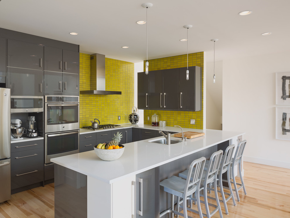 Foto di una cucina minimal con lavello sottopiano, ante lisce, ante grigie, paraspruzzi giallo, elettrodomestici in acciaio inossidabile e parquet chiaro