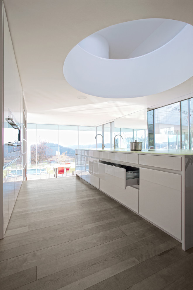 Exempel på ett modernt kök, med släta luckor, vita skåp, bänkskiva i glas, rostfria vitvaror och en köksö