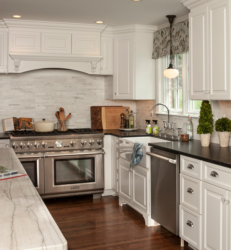 Klassisk inredning av ett mellanstort l-kök, med en rustik diskho, luckor med upphöjd panel, vita skåp, grått stänkskydd, stänkskydd i stickkakel, rostfria vitvaror, mörkt trägolv och en köksö