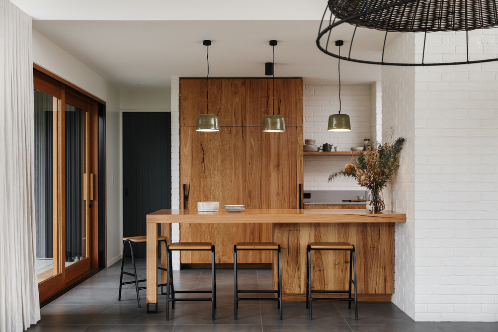 Zweizeilige Moderne Küche mit flächenbündigen Schrankfronten, hellbraunen Holzschränken, Küchenrückwand in Weiß, Rückwand aus Backstein, Kücheninsel und grauem Boden in Adelaide