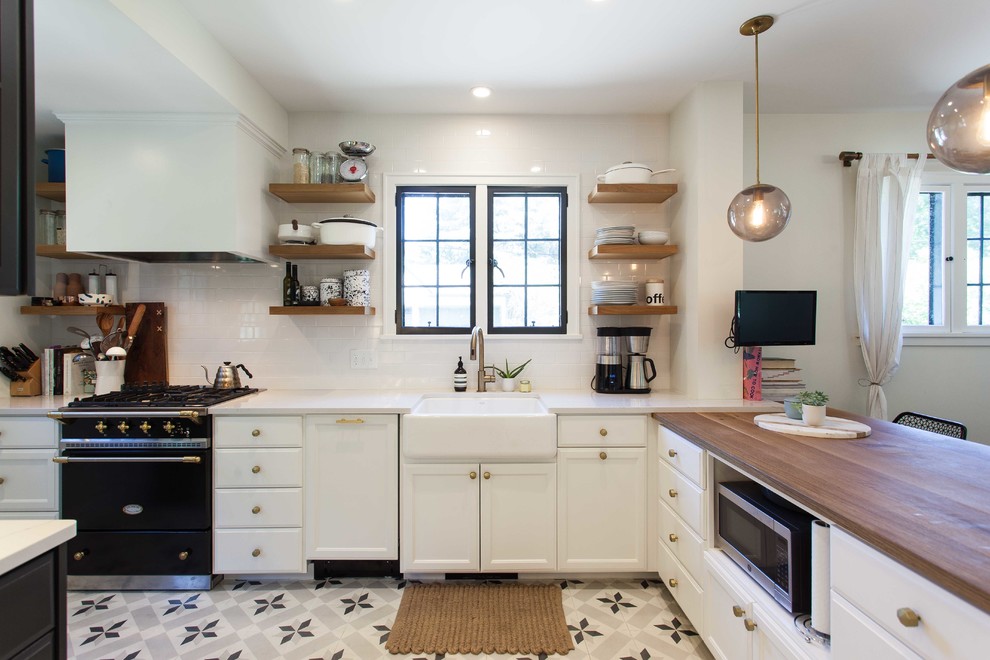 Immagine di una cucina minimalista di medie dimensioni con lavello stile country, ante con riquadro incassato, ante nere, top in legno, elettrodomestici da incasso, pavimento in cementine e penisola