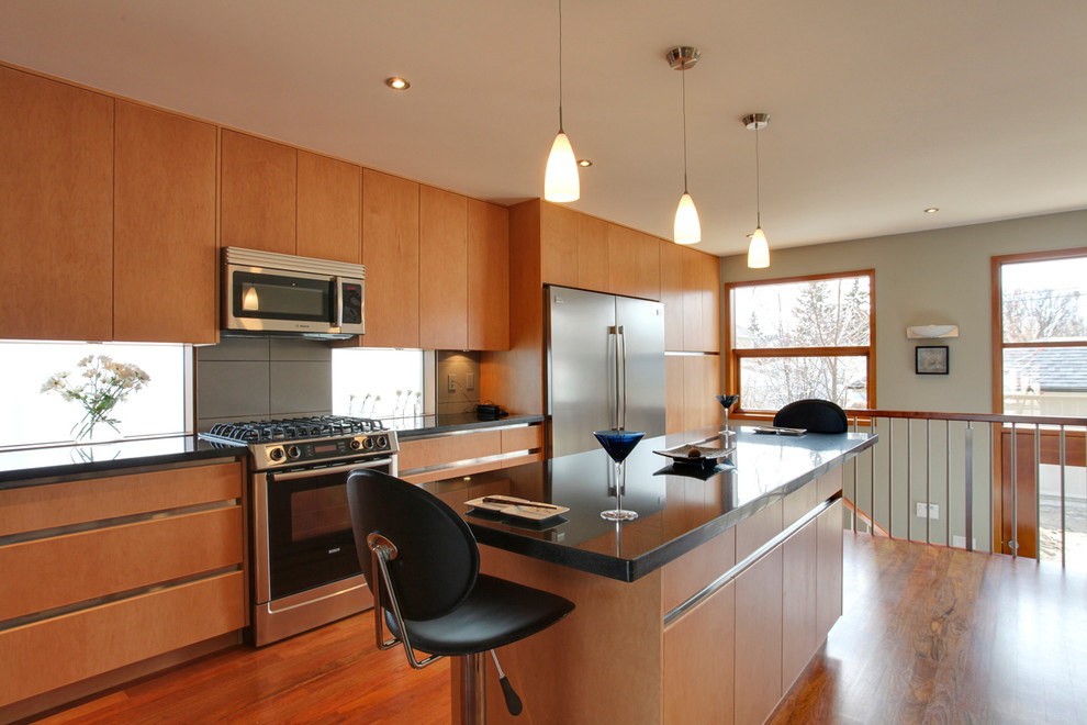 Photo of a large modern l-shaped kitchen/diner in Calgary with a submerged sink, flat-panel cabinets, light wood cabinets, composite countertops, grey splashback, porcelain splashback, stainless steel appliances, light hardwood flooring, an island and brown floors.