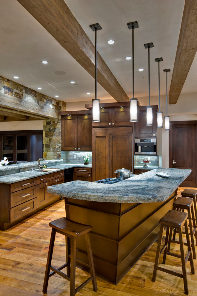 Inspiration for a large rustic medium tone wood floor eat-in kitchen remodel in Denver with an undermount sink, recessed-panel cabinets, dark wood cabinets, granite countertops, gray backsplash, stone tile backsplash, stainless steel appliances and an island