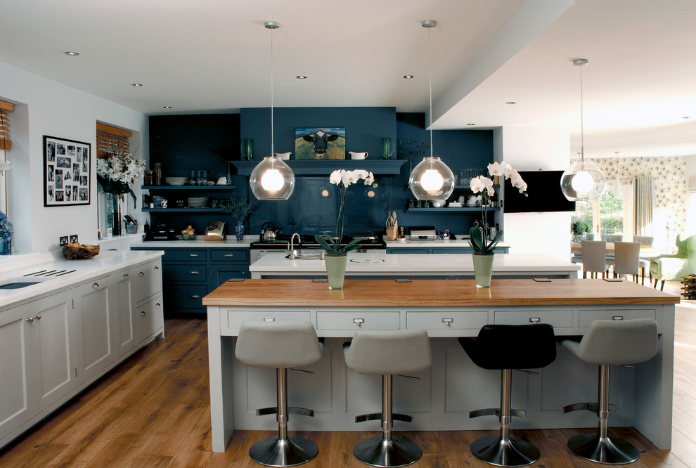 Minimalistisk inredning av ett kök, med skåp i shakerstil, blått stänkskydd, glaspanel som stänkskydd och flera köksöar