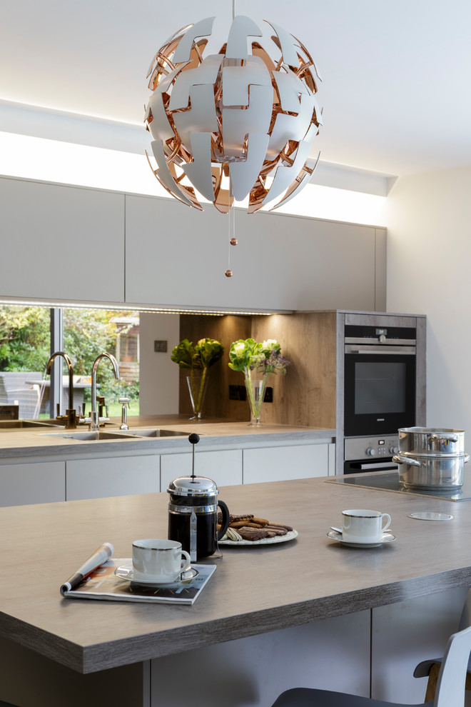 Moderne Wohnküche mit grauen Schränken, Küchenrückwand in Grau, Rückwand aus Spiegelfliesen, Kücheninsel, Doppelwaschbecken, Laminat-Arbeitsplatte und Küchengeräten aus Edelstahl in Surrey