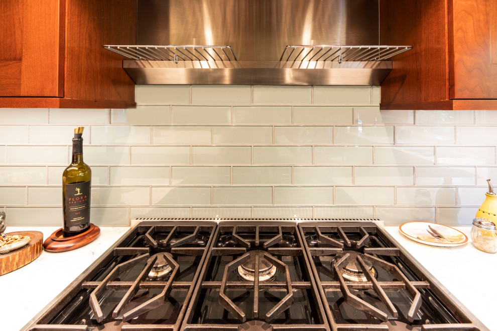 Inredning av ett klassiskt mellanstort vit vitt kök, med en undermonterad diskho, skåp i shakerstil, bruna skåp, bänkskiva i kvarts, grått stänkskydd, stänkskydd i glaskakel, integrerade vitvaror, ljust trägolv, en köksö och brunt golv