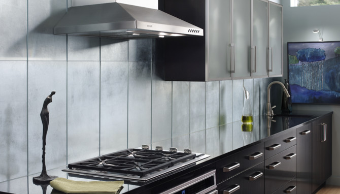 На фото: кухня в стиле модернизм с черными фасадами, синим фартуком, техникой из нержавеющей стали и паркетным полом среднего тона с