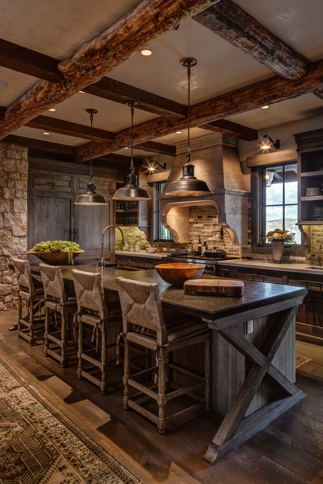 Photo of a rustic l-shaped kitchen in Salt Lake City with an island, brown floors, a belfast sink, recessed-panel cabinets, dark wood cabinets, grey splashback, integrated appliances and dark hardwood flooring.