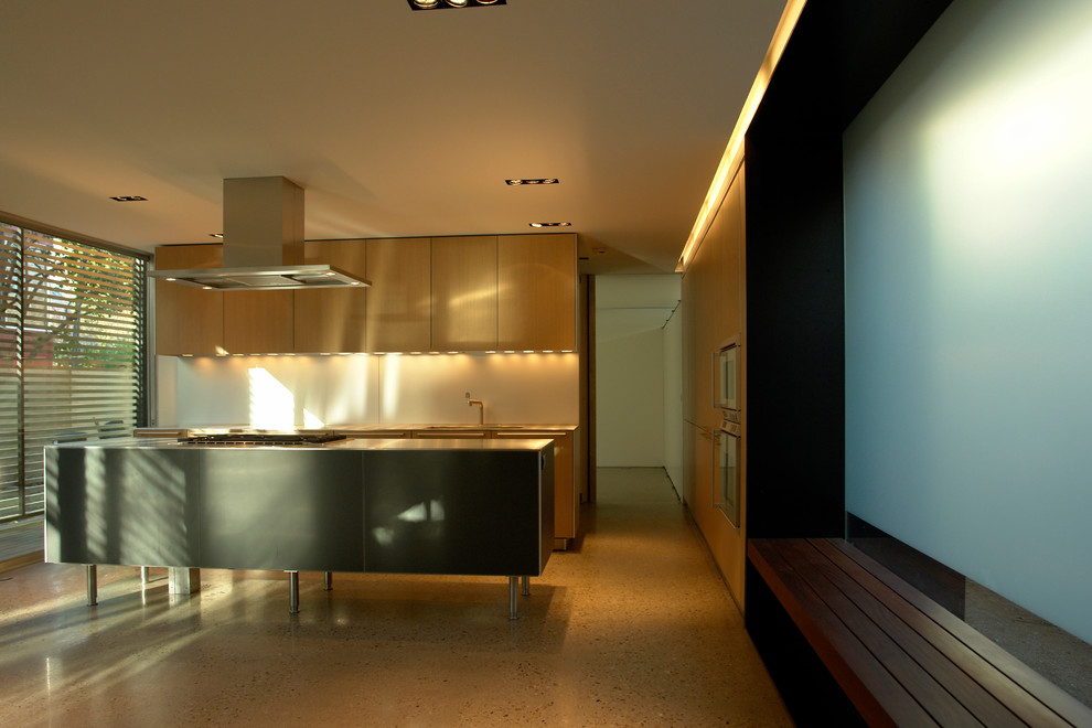 Immagine di una cucina minimal di medie dimensioni con ante lisce, ante in legno chiaro, paraspruzzi bianco, elettrodomestici da incasso e pavimento in cemento