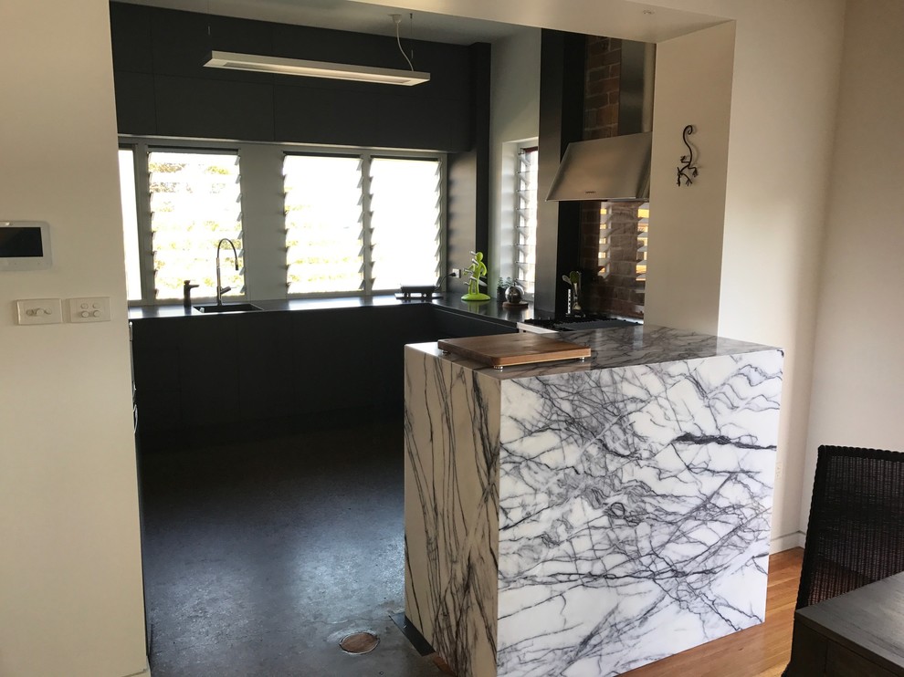 Immagine di un cucina con isola centrale industriale di medie dimensioni con lavello sottopiano, top in marmo, paraspruzzi con lastra di vetro e pavimento in cemento