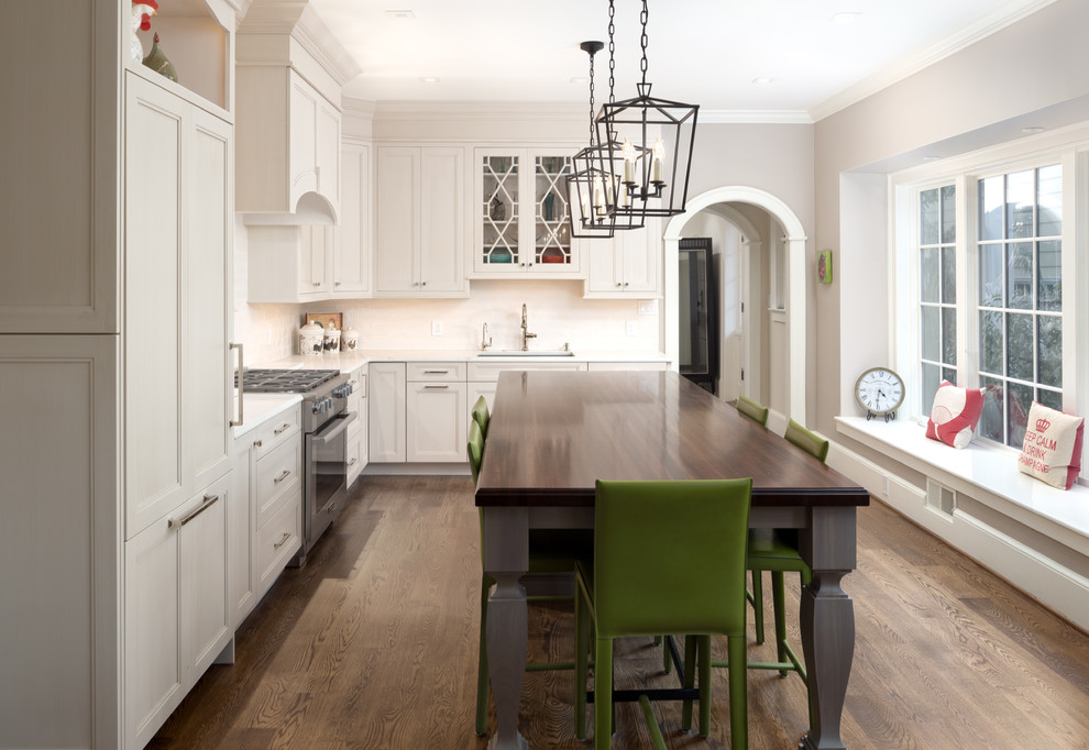 This is an example of a traditional l-shaped kitchen in DC Metro with a submerged sink, recessed-panel cabinets, white cabinets, white splashback, stainless steel appliances, medium hardwood flooring and an island.