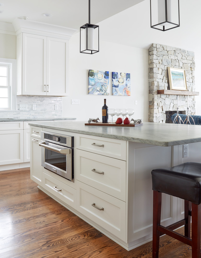 Foto på ett vintage kök, med en undermonterad diskho, luckor med infälld panel, vita skåp, granitbänkskiva, grått stänkskydd, stänkskydd i mosaik, integrerade vitvaror, mellanmörkt trägolv, en köksö och brunt golv