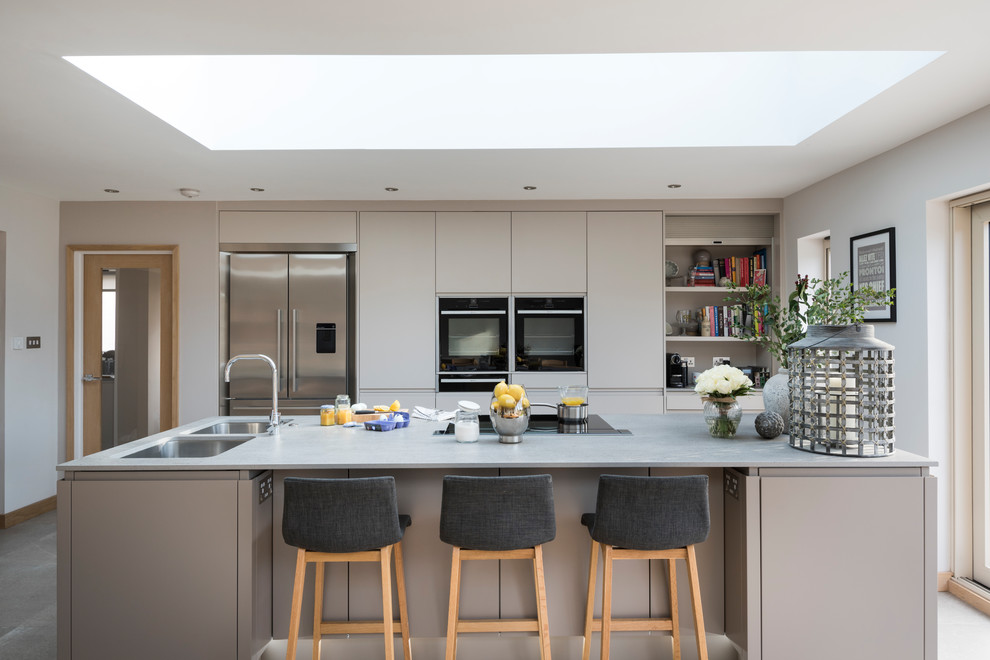Bild på ett stort funkis grå linjärt grått kök med öppen planlösning, med en dubbel diskho, bänkskiva i kvartsit, rostfria vitvaror, en halv köksö och brunt golv