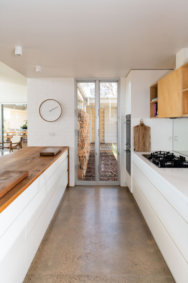 Inredning av ett modernt mellanstort brun brunt kök, med en dubbel diskho, vita skåp, träbänkskiva, stänkskydd med metallisk yta, spegel som stänkskydd, vita vitvaror, betonggolv, en köksö och grått golv