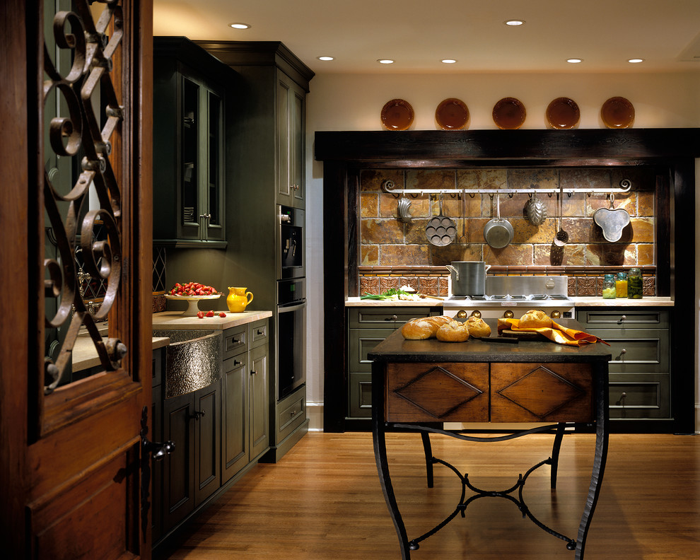 Foto på ett stort rustikt kök, med en rustik diskho, luckor med infälld panel, gröna skåp, bänkskiva i kalksten, flerfärgad stänkskydd, stänkskydd i stenkakel, integrerade vitvaror, mellanmörkt trägolv och en köksö