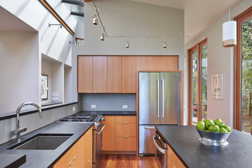 Exempel på ett modernt l-kök, med en undermonterad diskho, släta luckor, skåp i mellenmörkt trä, grått stänkskydd, rostfria vitvaror, mellanmörkt trägolv och en köksö