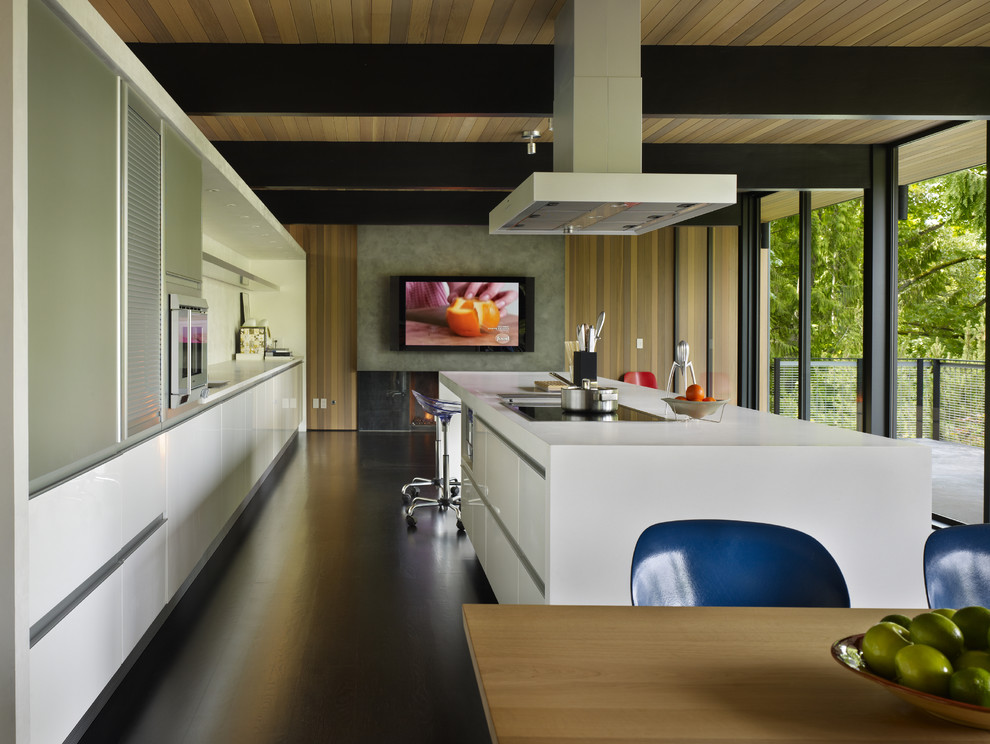На фото: параллельная кухня среднего размера в стиле модернизм с обеденным столом, плоскими фасадами, белыми фасадами, врезной мойкой, столешницей из кварцита, белым фартуком, темным паркетным полом и островом с