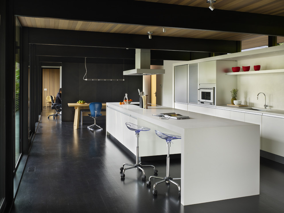 Exempel på ett mellanstort modernt kök, med släta luckor, vita skåp, en undermonterad diskho, bänkskiva i kvartsit, vitt stänkskydd, mörkt trägolv, en köksö och svart golv