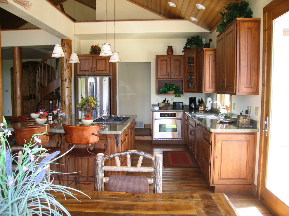 Exemple d'une cuisine américaine montagne en L et bois brun avec un évier 2 bacs, un placard avec porte à panneau surélevé, un plan de travail en granite, un électroménager en acier inoxydable, un sol en bois brun et îlot.