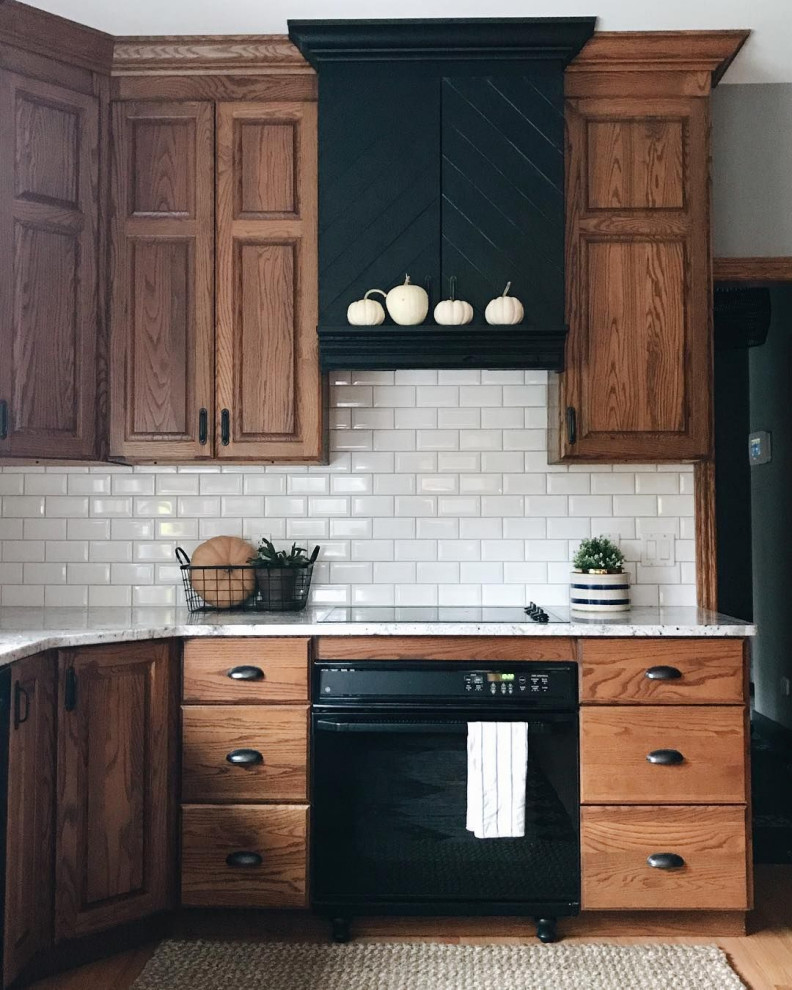 Foto de cocina clásica de tamaño medio con fregadero bajoencimera, armarios con paneles con relieve, puertas de armario de madera oscura, encimera de cuarzo compacto, salpicadero blanco, salpicadero de azulejos tipo metro, electrodomésticos negros, suelo de madera clara, suelo marrón y encimeras blancas