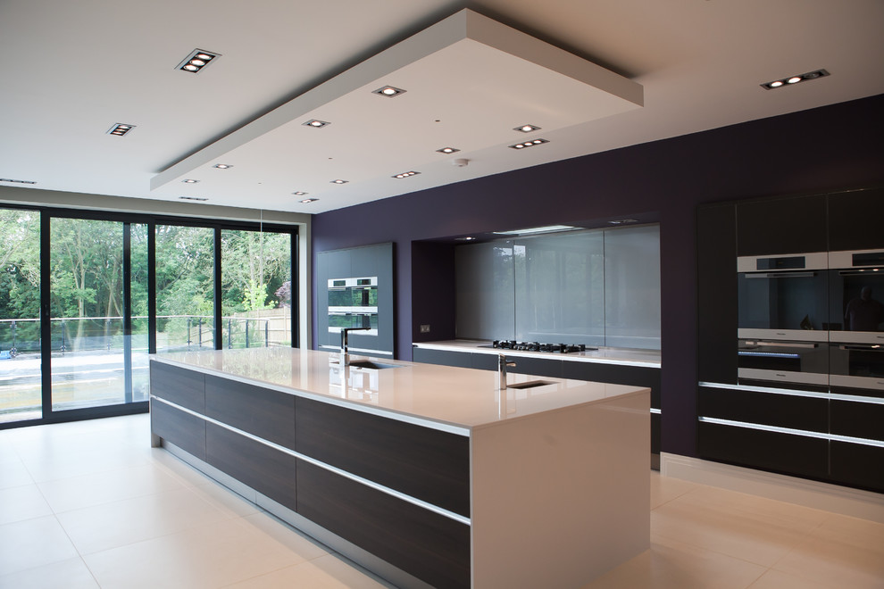 This is an example of a large contemporary kitchen in Hertfordshire with a submerged sink, flat-panel cabinets, dark wood cabinets, grey splashback, glass sheet splashback and an island.