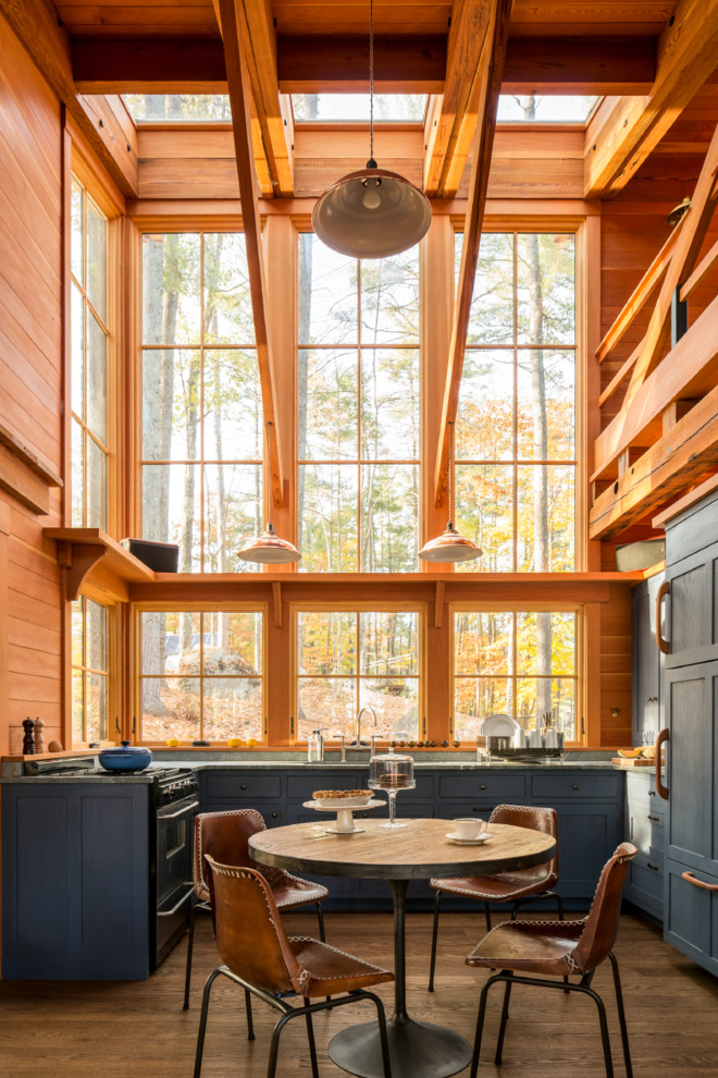 Mittelgroße Urige Wohnküche ohne Insel in U-Form mit Schrankfronten im Shaker-Stil, blauen Schränken, Speckstein-Arbeitsplatte, Elektrogeräten mit Frontblende, braunem Boden, Rückwand-Fenster und dunklem Holzboden in Portland Maine