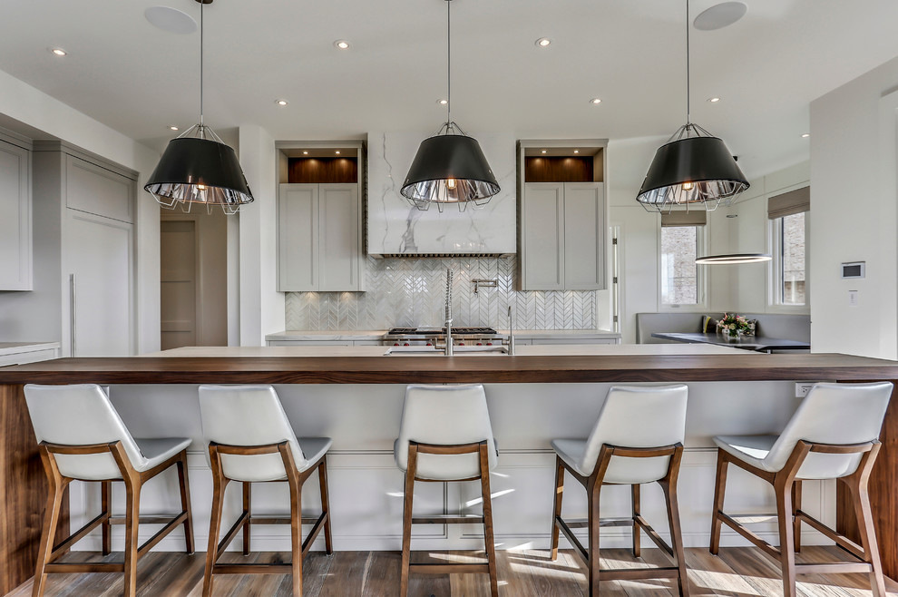 Trendy u-shaped kitchen photo in Calgary with wood countertops, an island, an undermount sink, recessed-panel cabinets, gray cabinets, gray backsplash and paneled appliances