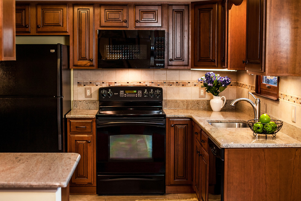 Bild på ett avskilt, litet vintage l-kök, med en undermonterad diskho, luckor med upphöjd panel, skåp i mörkt trä, granitbänkskiva, brunt stänkskydd, stänkskydd i keramik, svarta vitvaror och en halv köksö