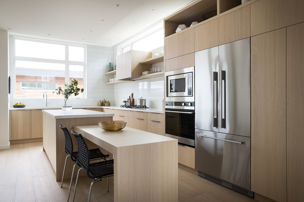 Photo of a small contemporary l-shaped kitchen/diner in Vancouver with flat-panel cabinets, wood worktops, white splashback, porcelain splashback, stainless steel appliances, light hardwood flooring, an island, beige floors, light wood cabinets and white worktops.