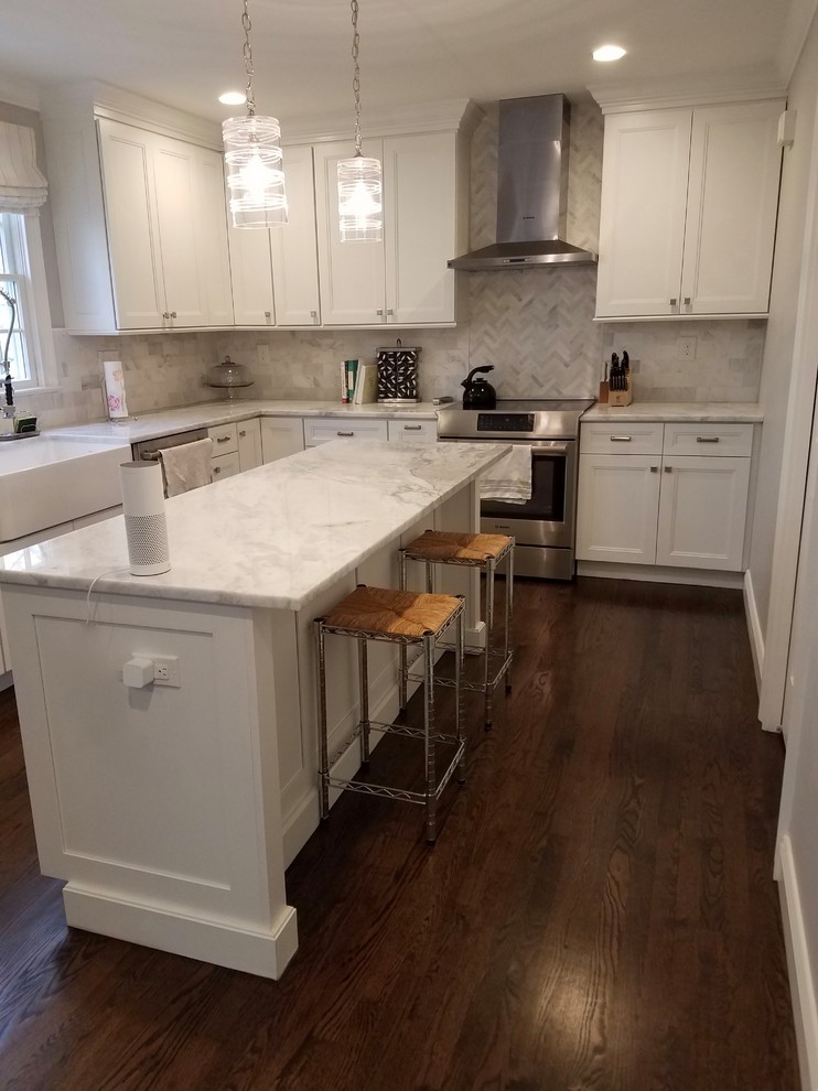 Example of a mid-sized transitional l-shaped medium tone wood floor and brown floor enclosed kitchen design in New York with a farmhouse sink, recessed-panel cabinets, white cabinets, marble countertops, gray backsplash, marble backsplash, stainless steel appliances and an island