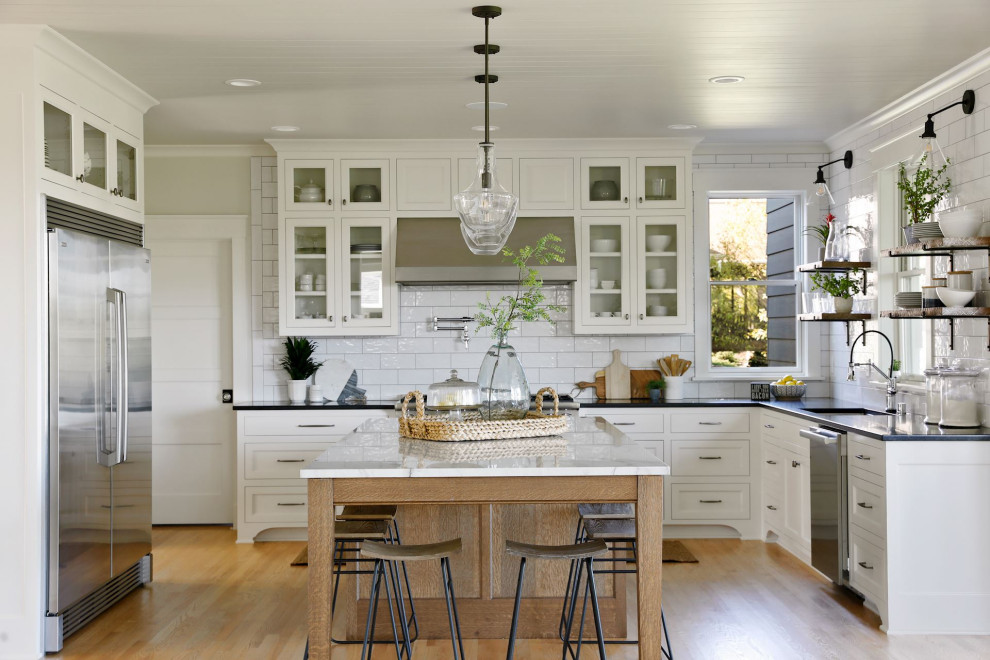 Design ideas for a coastal u-shaped kitchen in Minneapolis with white cabinets, quartz worktops, metro tiled splashback, stainless steel appliances, light hardwood flooring, an island, a single-bowl sink, glass-front cabinets, white splashback, beige floors, black worktops and a timber clad ceiling.